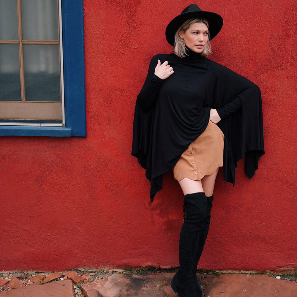 Black Standard Everyday Poncho Girl Outside Against Red Wall Wearing Skirt and Boots