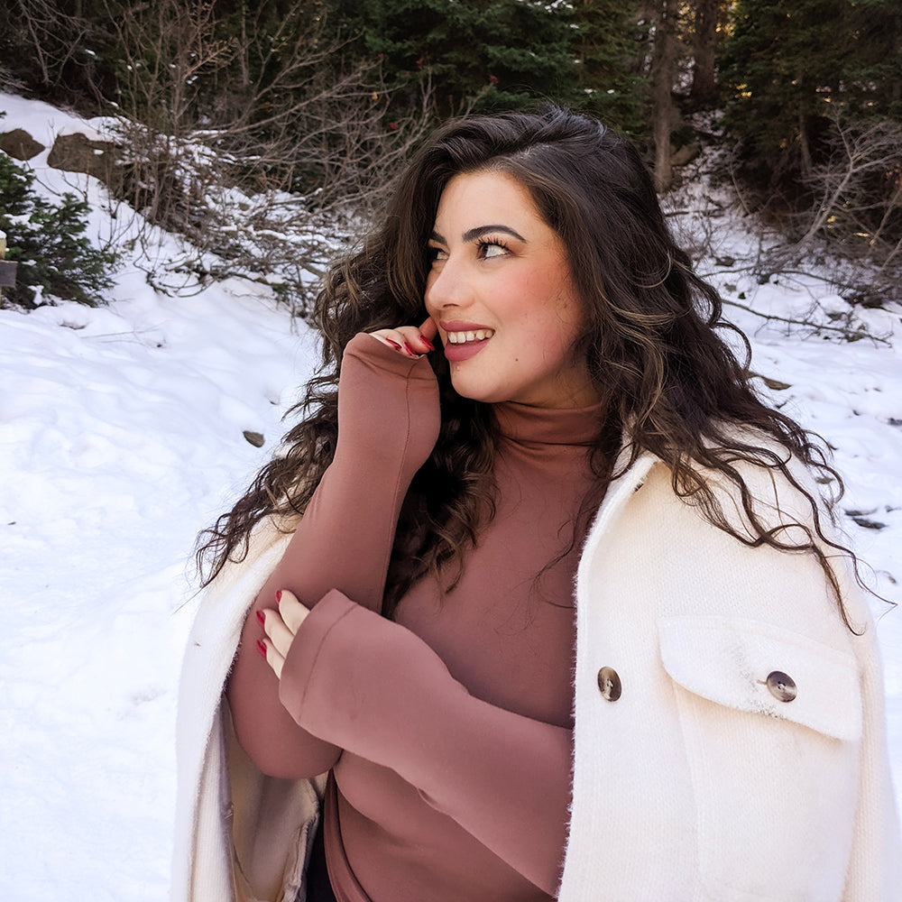 Woman Outside With Snow Wearing A White Jacket And Copper Turtleneck