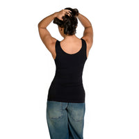 A woman viewed from behind wearing a black tank top and blue jeans, with her hands raised in her hair, against a plain white background.