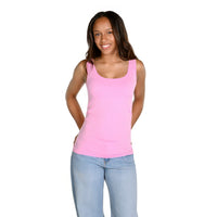 A woman modeling a bubblegum pink sleeveless scoop-neck tank top paired with light blue jeans, standing against a solid white background.