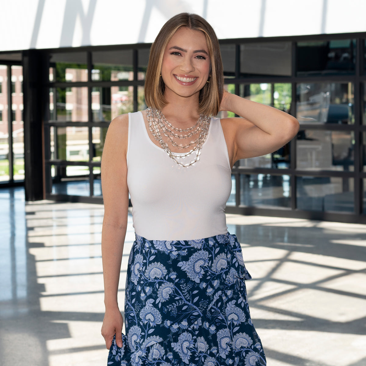 Woman Standing outside wearing a White Basic Tank Top with a blue and white skirt and a clear beaded necklace