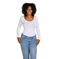 A woman with curly black hair wearing a fitted white long-sleeve scoop-neck top and light blue jeans, standing against a plain white background.