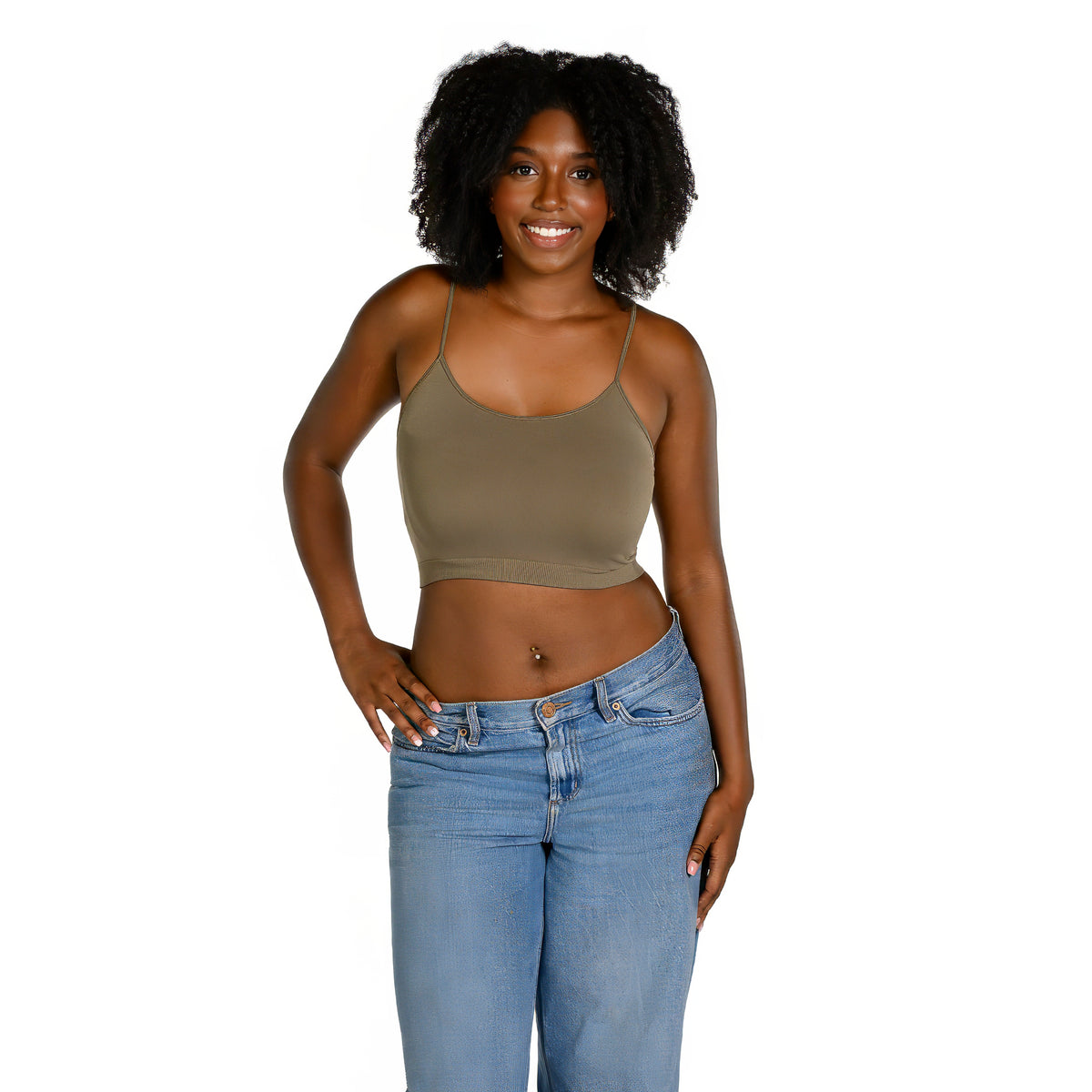 A woman with curly black hair wearing a fitted army green bralette and light blue jeans, standing against a solid white background.