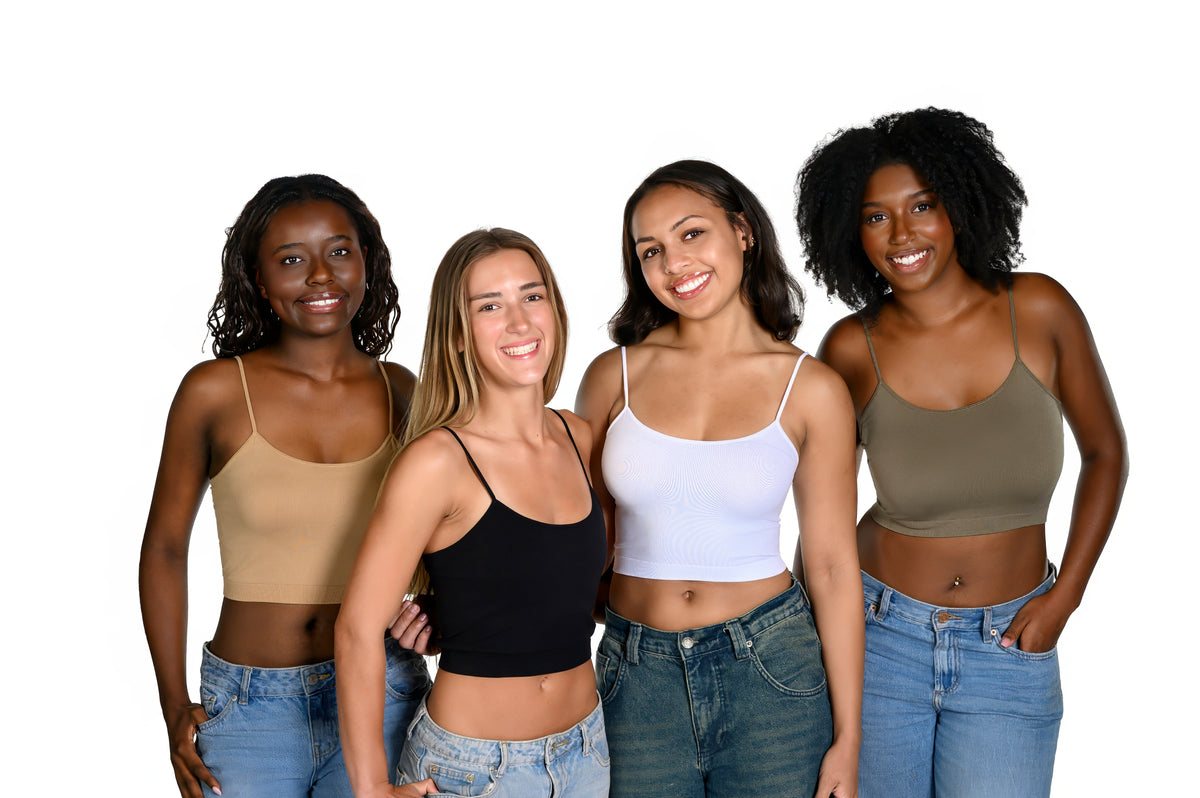 Four women of diverse ethnicities standing together and smiling, wearing different colored bralettes (brown sugar, black, white, and army green) paired with blue jeans, against a solid white background.