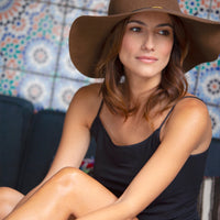 Woman wearing brimmed hat and a Black Basic Camisole against a tile wall
