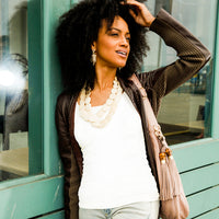 Woman in white basic tank top leaning against green wall outside.