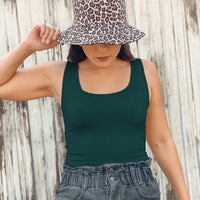 Woman looking down wearing a forest basic tank top and a leopard print hat