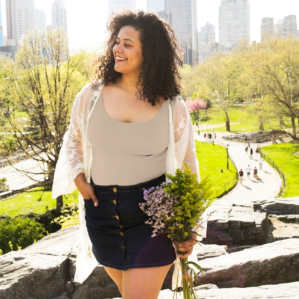 Woman standing in a park in a city wearing a stone plus basic tank top holding flowers